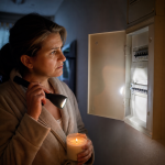 Personne tenant bougie et lampe torche devant tableau électrique